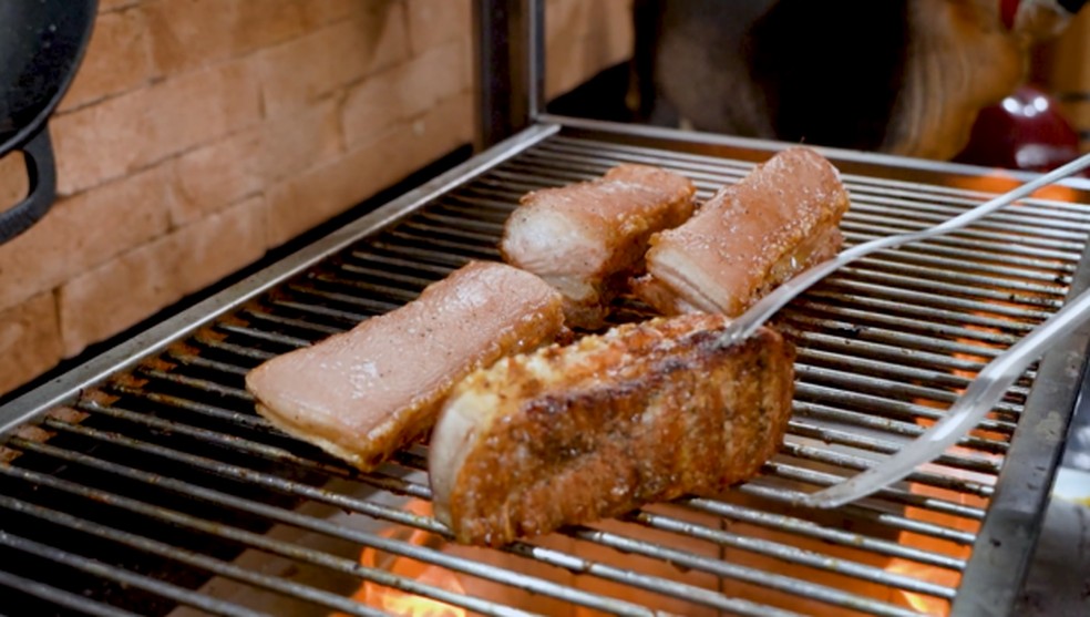 Panceta sendo assada na grelha, mostrando o lado da carne com uma cor dourada apetitosa.